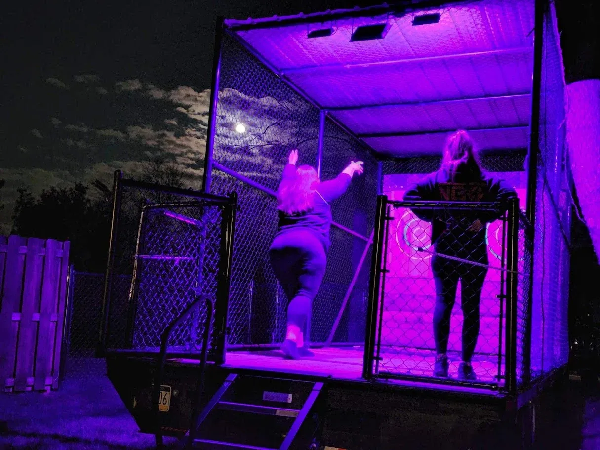 Two guests throwing axes at night under purple lights